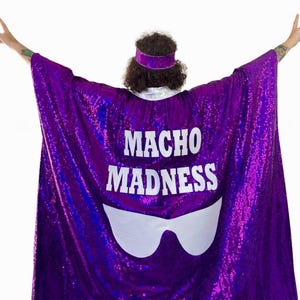 May include: A vibrant purple sequined cape emblazoned with the white text "MACHO MADNESS". Below the text is a white sunglasses graphic. A matching purple sequined headband is also visible.