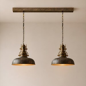 May include: Two industrial-style pendant lights with a bronze finish. Each light has a domed shade and is suspended by a chain from a rectangular bronze-colored bar. The interior of the shades have a gold finish.