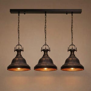 May include: Three-light pendant fitting with a dark bronze finish. Each light has a bell-shaped shade with a ribbed design and a warm, golden interior. The lights hang from chains attached to a rectangular bar.