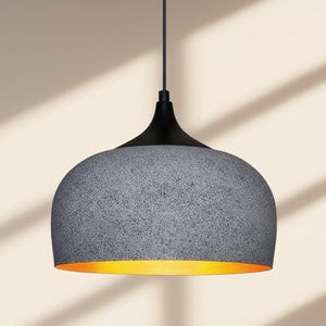 Könnte beinhalten: Moderne Pendelleuchte mit strukturiertem, grauem Schirm und schwarzem Oberteil. Das Innere des Schirms strahlt ein warmes, gelbes Licht aus. Die Leuchte hängt an einem schwarzen Kabel, ideal für Küche oder Esszimmer.