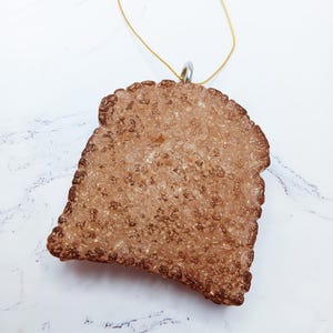 May include: A decorative ornament with a textured, brown, irregular shape. The ornament has a gold string for hanging. The surface has a bubbly appearance with a darker brown border. The ornament is likely for holiday or seasonal decor.