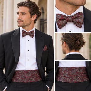 May include: A burgundy cummerbund and matching bow tie featuring a detailed paisley pattern. The set is worn with a crisp white tuxedo shirt, a black tuxedo jacket with satin lapels, and a small matching pocket square tucked into the jacket.