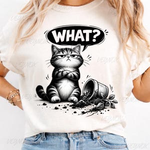 Könnte beinhalten: Weißes T-Shirt mit einer Illustration einer grimmigen, schwarz-grauen Cartoon-Katze mit verschränkten Armen und einem Sprechblasen-Text "WHAT?". Ein umgestürzter Blumentopf und Erde ergänzen das Design, eine humorvolle Illustration.