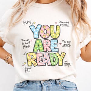 Puede incluir: Camiseta color crema con las palabras "YOU ARE READY" en letras de bloque coloridas. La camiseta tiene texto adicional que incluye "Test Day", "You can do hard things" y "Do your best."