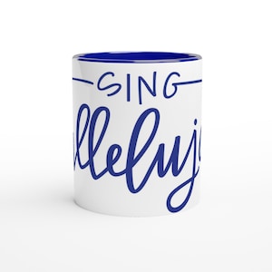 Puede incluir: Taza de cerámica blanca con interior azul y las palabras "-SING hallelujah" en escritura azul. La taza es cilíndrica y tiene un acabado brillante, adecuada para bebidas frías o calientes.