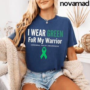 Op de afbeelding: Marineblauw T-shirt met de tekst "I Wear Green For My Warrior" in wit en groen, met een groene lintafbeelding. Het shirt bevat ook de tekst "Cerebral Palsy Awareness".