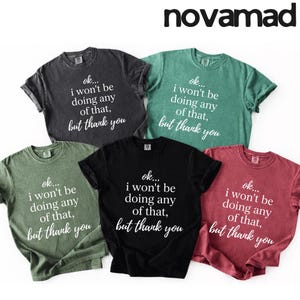 May include: Five short-sleeved t-shirts in various colors: charcoal, green, black, red, and olive. Each shirt features the text "ok... I won't be doing any of that, but thank you" in white script. The brand name "novamad" is at the top.