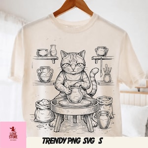 May include: Cream-colored t-shirt featuring a black and white illustration of a cat working at a pottery wheel. The cat wears an apron and is surrounded by pottery and bags of clay. The text "TRENDY PNG SVG S" is at the bottom.