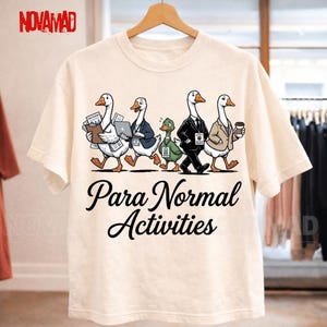 Puede incluir: Una camiseta de color crema con un gráfico de cinco gansos vestidos con ropa de negocios, incluyendo trajes y tarjetas de identificación, uno sosteniendo una computadora portátil y otro una taza de café. Debajo, el texto dice Para Normal Activities.