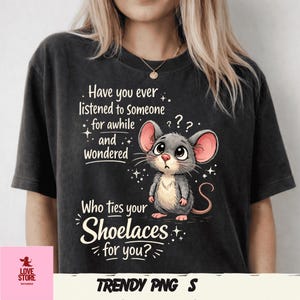 May include: Dark gray t-shirt with a graphic of a cartoon mouse and the text "Have you ever listened to someone for awhile and wondered Who ties your Shoelaces for you?" The shirt also has the text "TRENDY PNG S".