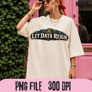 Könnte beinhalten: Ein cremefarbenes Kurzarm-T-Shirt mit einem Grafikdesign, das eine Krone und den Text "LET DATA REIGN" in einer dunklen, verzierten Schrift zeigt. Das Design enthält blaue und goldene Akzente und das Shirt hat eine lockere Passform.