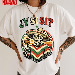 Può includere: Una t-shirt bianca a maniche corte con la grafica di uno scheletro che indossa un sombrero e un poncho a righe, mentre tiene in mano una maraca. Il testo sopra la grafica recita ¿Y SI SÍ? in verde, giallo e rosso. Il design è su sfondo circolare.