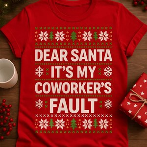 May include: A red Christmas-themed t-shirt with the text "DEAR SANTA IT'S MY COWORKER'S FAULT" in white. The design includes snowflakes and Christmas trees in green and white, creating a festive holiday look.