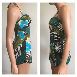Pode incluir: Fato de banho de uma pe&ccedil;a com gola halter e estampa floral e folhagem tropical. O fato de banho apresenta um fundo preto com um padr&atilde;o de listras de zebra brancas, folhas verdes e flores azuis e amarelas.