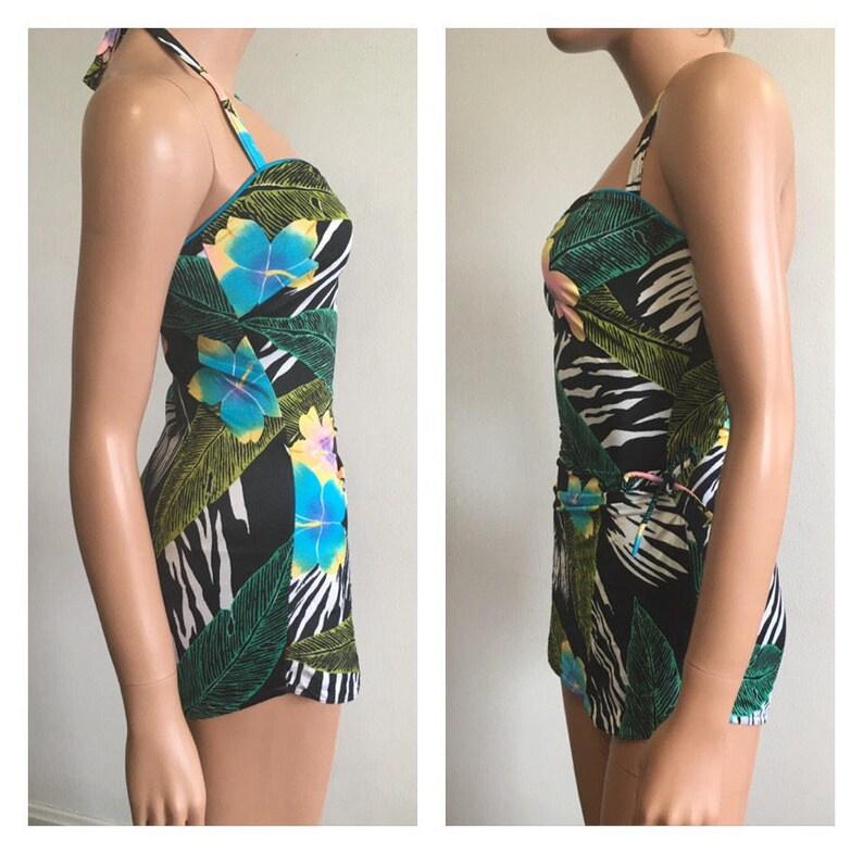 Pode incluir: Fato de banho de uma pe&ccedil;a com gola halter e estampa floral e folhagem tropical. O fato de banho apresenta um fundo preto com um padr&atilde;o de listras de zebra brancas, folhas verdes e flores azuis e amarelas.