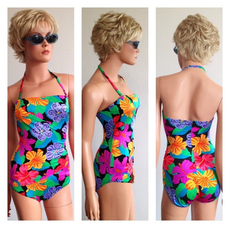 Peut inclure: Un maillot de bain une pi&egrave;ce avec un motif floral vibrant. Le maillot de bain pr&eacute;sente un fond noir avec de grandes fleurs color&eacute;es dans les tons de rose, orange, jaune, bleu et vert. Il a un col halter et une coupe ajust&eacute;e.