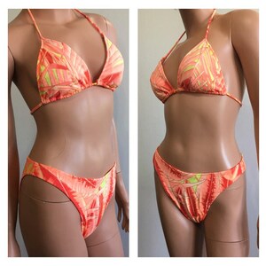 Pu&ograve; includere: Un bikini a due pezzi con un vivace motivo a foglie arancioni e gialle. La parte superiore &egrave; a triangolo con spalline sottili e la parte inferiore &egrave; a taglio classico. Il costume da bagno &egrave; esposto su un manichino.