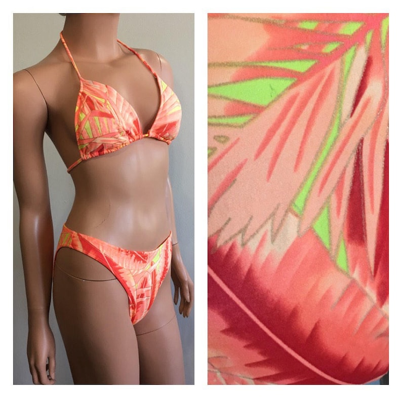 Pu&ograve; includere: Un bikini a due pezzi nei toni dell'arancione, del rosa e del giallo. Il top del bikini con collo all'americana e gli slip a vita alta presentano un motivo a foglie tropicali. Il costume da bagno &egrave; esposto su un manichino.