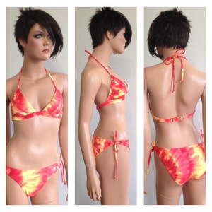 Peut inclure: Bikini tie-dye aux tons de rouge, jaune et orange. Le haut de style dos nu et le bas ont des cordons. Le bikini est présenté sur un mannequin.