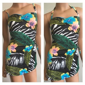 Pode incluir: Um fato de banho com estampa de zebra a preto e branco com um design floral tropical. O fato de banho apresenta um design sem al&ccedil;as com al&ccedil;as finas e uma saia envolvente. O padr&atilde;o floral inclui flores azuis, amarelas e rosas e folhas verdes.