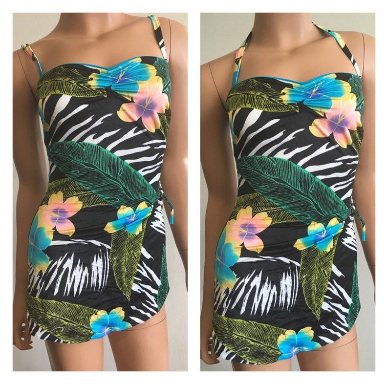Pode incluir: Um fato de banho com estampa de zebra a preto e branco com um design floral tropical. O fato de banho apresenta um design sem al&ccedil;as com al&ccedil;as finas e uma saia envolvente. O padr&atilde;o floral inclui flores azuis, amarelas e rosas e folhas verdes.