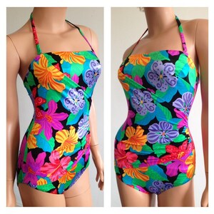 Peut inclure: Un maillot de bain une pi&egrave;ce avec un motif floral vibrant. Le maillot de bain pr&eacute;sente un fond noir avec de grandes fleurs color&eacute;es dans les tons de rose, orange, jaune, bleu et violet. Il a un col licou et un devant crois&eacute;.