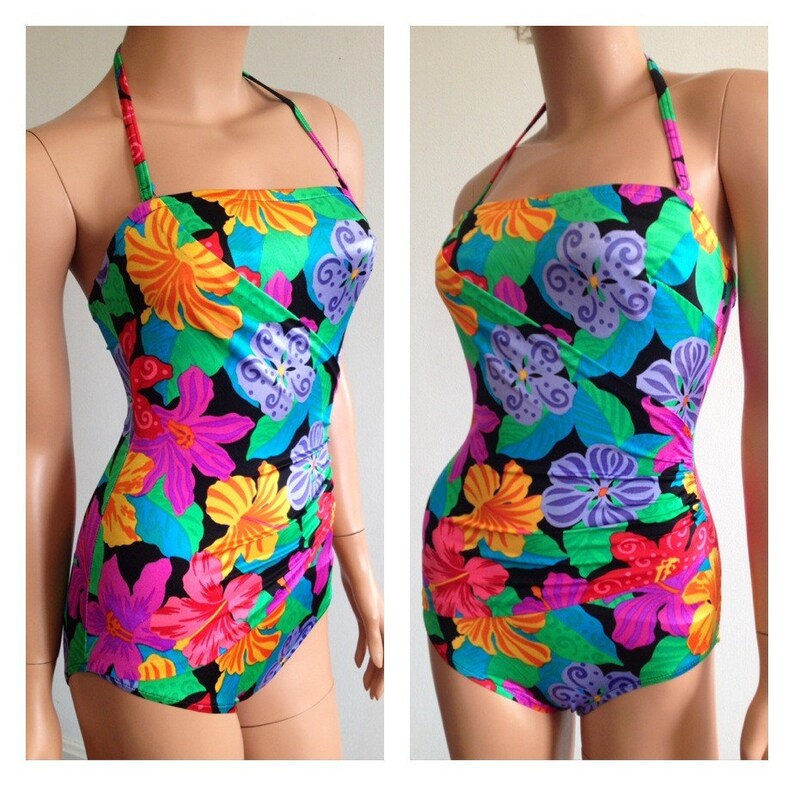 Peut inclure: Un maillot de bain une pi&egrave;ce avec un motif floral vibrant. Le maillot de bain pr&eacute;sente un fond noir avec de grandes fleurs color&eacute;es dans les tons de rose, orange, jaune, bleu et violet. Il a un col licou et un devant crois&eacute;.