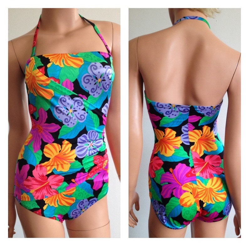 Peut inclure: Un maillot de bain une pi&egrave;ce avec un motif floral vibrant. Le maillot de bain pr&eacute;sente un col licou et un fond noir avec de grandes fleurs color&eacute;es dans les tons orange, rose, violet et bleu. Le design comprend des feuilles vertes.