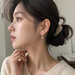 May include: Delicate gold earrings with three clear, sparkling stones. The earrings dangle gracefully, reflecting light. The top two stones are small and round, while the bottom stone is a teardrop shape. These earrings are a classic accessory.