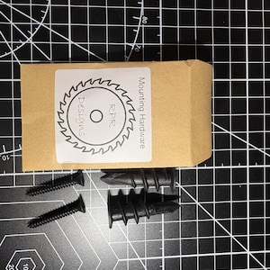 A complete installation kit featuring two black self-drilling drywall anchors and two matching black screws in a professional packet.