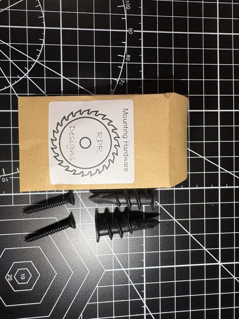 A complete installation kit featuring two black self-drilling drywall anchors and two matching black screws in a professional packet.