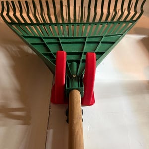 A universal garage storage hook holding a garden rake to demonstrate versatility for different long-handled tools.