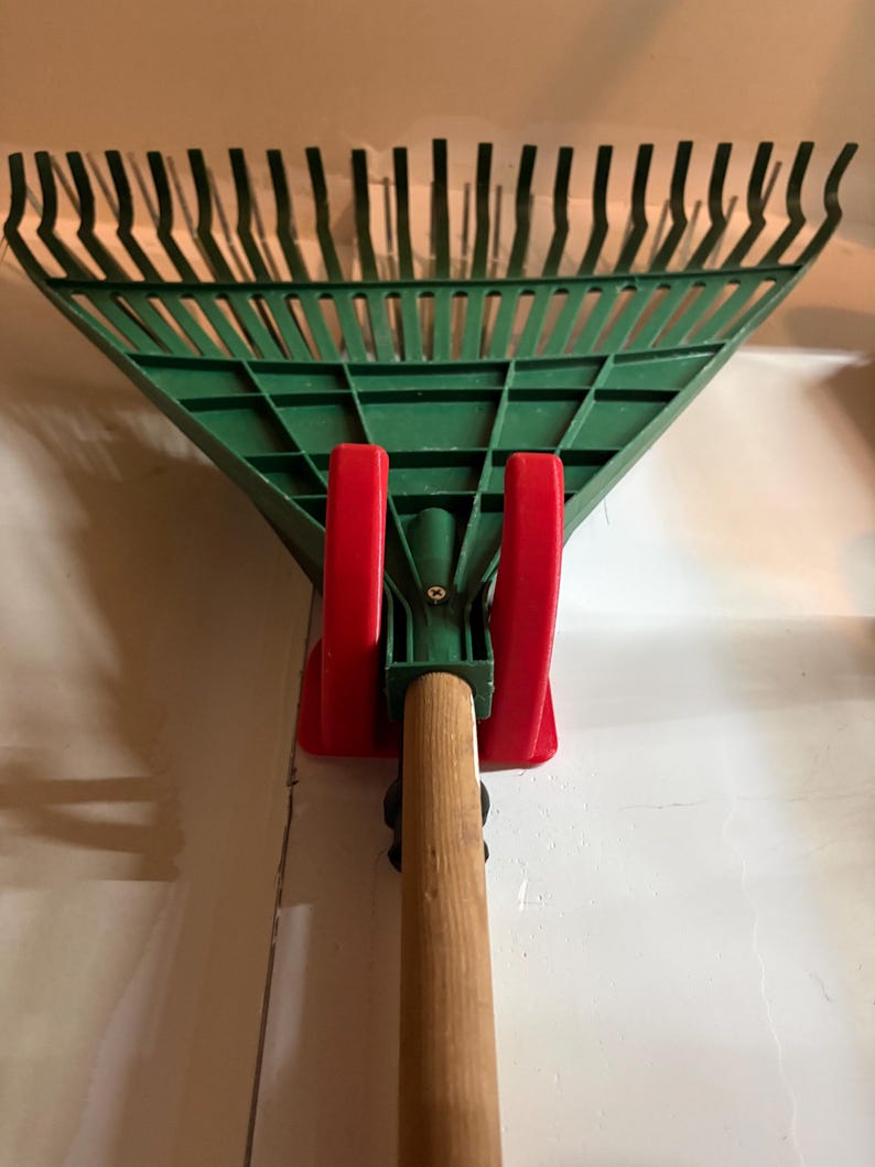 A universal garage storage hook holding a garden rake to demonstrate versatility for different long-handled tools.