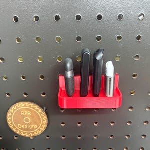 Front view of a red pegboard-mounted USB drive holder containing various flash drives and security keys, showcasing the 15mm front lip that keeps devices securely in place.