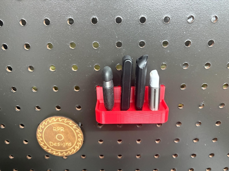 Front view of a red pegboard-mounted USB drive holder containing various flash drives and security keys, showcasing the 15mm front lip that keeps devices securely in place.