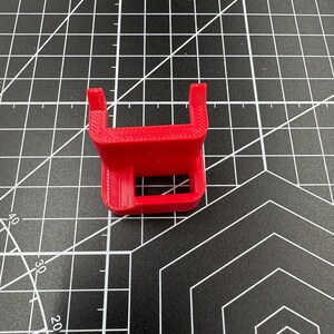 Top-down view of a red 3D-printed caliper mount on a black grid mat, highlighting the precise 17mm internal slot and 4mm pegs.