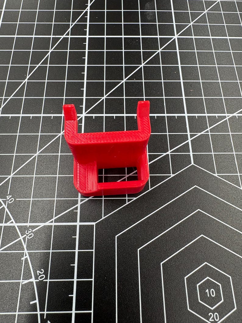 Top-down view of a red 3D-printed caliper mount on a black grid mat, highlighting the precise 17mm internal slot and 4mm pegs.
