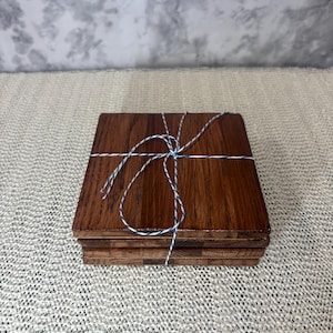 A stack of four handmade oak coasters tied with blue and white baker's twine, highlighting the layered wood and cork construction for gifting.