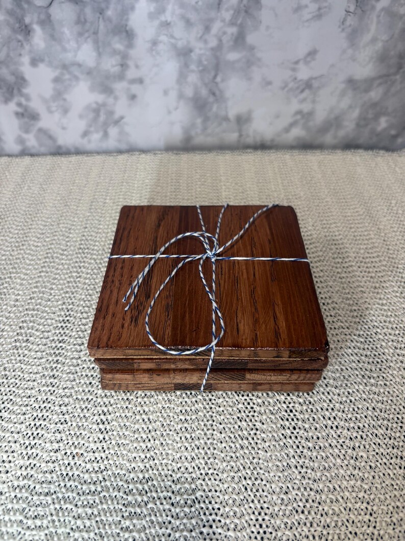 A stack of four handmade oak coasters tied with blue and white baker's twine, highlighting the layered wood and cork construction for gifting.
