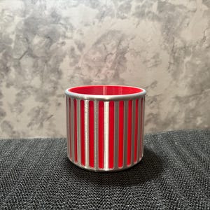 A futuristic silver pencil holder with a vibrant red interior and vertical slotted ribs on a grey textured surface.