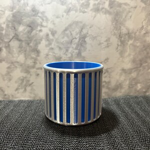 A modern silver pen cup with a bold blue interior, highlighting the architectural vertical slots and rounded top rim.