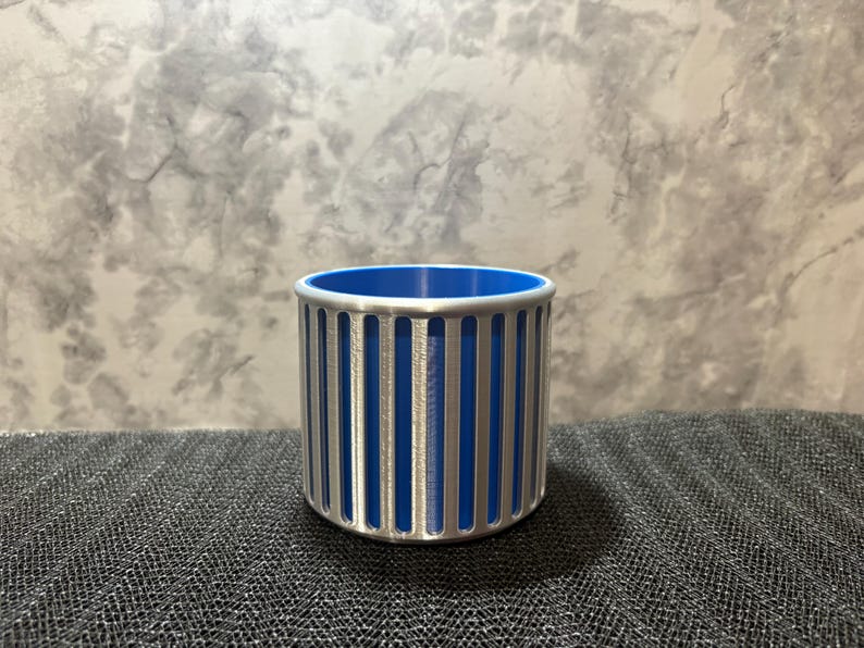 A modern silver pen cup with a bold blue interior, highlighting the architectural vertical slots and rounded top rim.