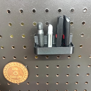 A black pegboard-mounted holder containing four different USB flash drives and security keys, showing a secure and organized workshop setup.
