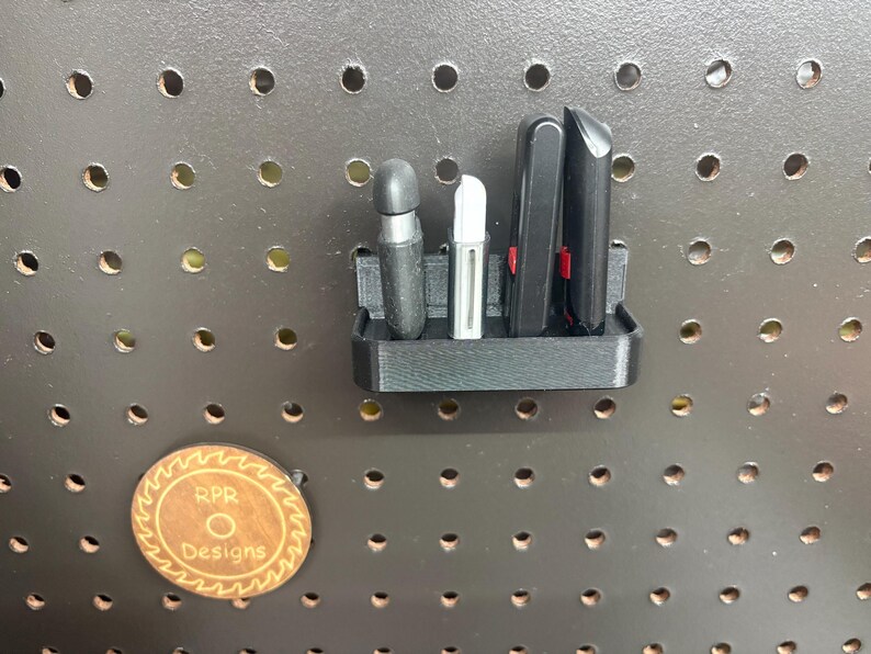 A black pegboard-mounted holder containing four different USB flash drives and security keys, showing a secure and organized workshop setup.