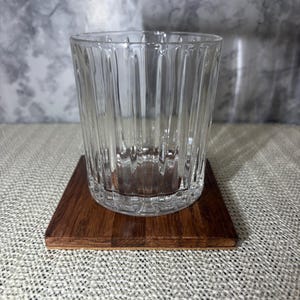 Close up of a single handcrafted square oak wood coaster with a clear fluted drinking glass on top, showing the natural wood grain and 3/8 inch thickness.