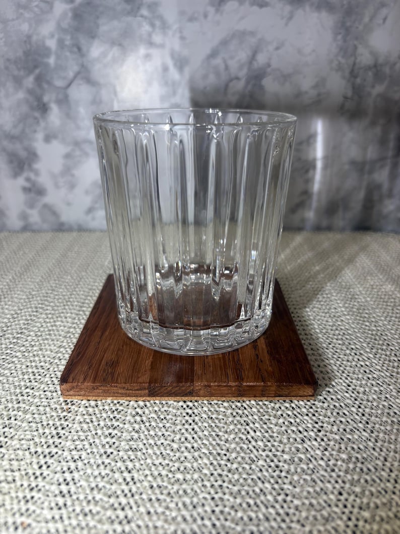 Close up of a single handcrafted square oak wood coaster with a clear fluted drinking glass on top, showing the natural wood grain and 3/8 inch thickness.