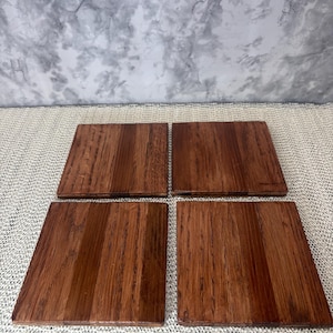 A set of four 4x4 inch solid oak wood coasters laid flat, showcasing the unique natural wood grain patterns and warm brown finish of the limited run set.