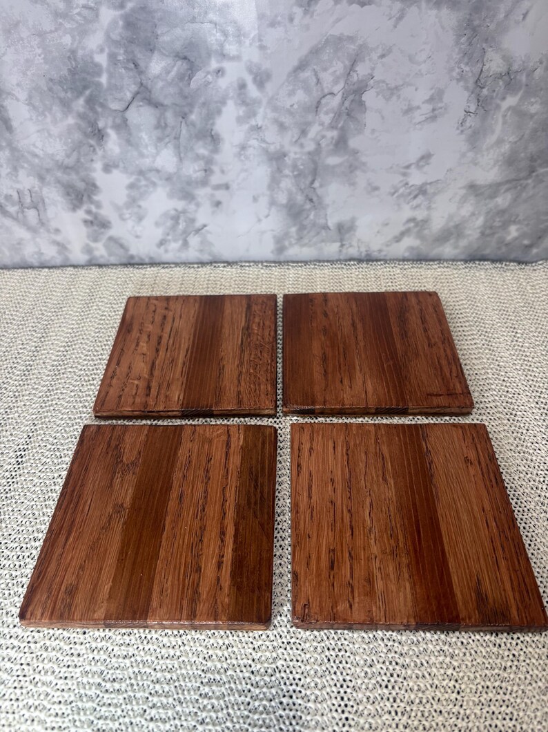 A set of four 4x4 inch solid oak wood coasters laid flat, showcasing the unique natural wood grain patterns and warm brown finish of the limited run set.