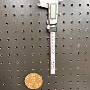 A digital caliper mounted in a sleek black 3D-printed pegboard holder, showing a low-profile organization solution for workshops.