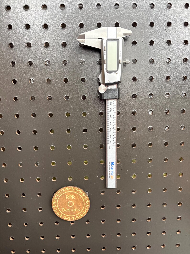 A digital caliper mounted in a sleek black 3D-printed pegboard holder, showing a low-profile organization solution for workshops.